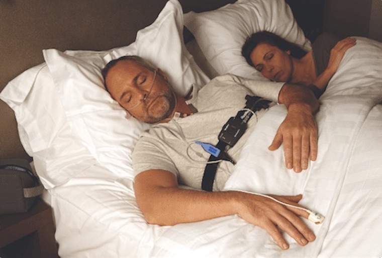 Man sleeping while wearing a sleep test chest strap and finger monitor
