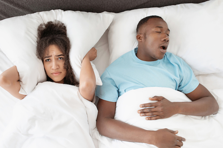 Man snoring in bed while woman covers ears with pillow